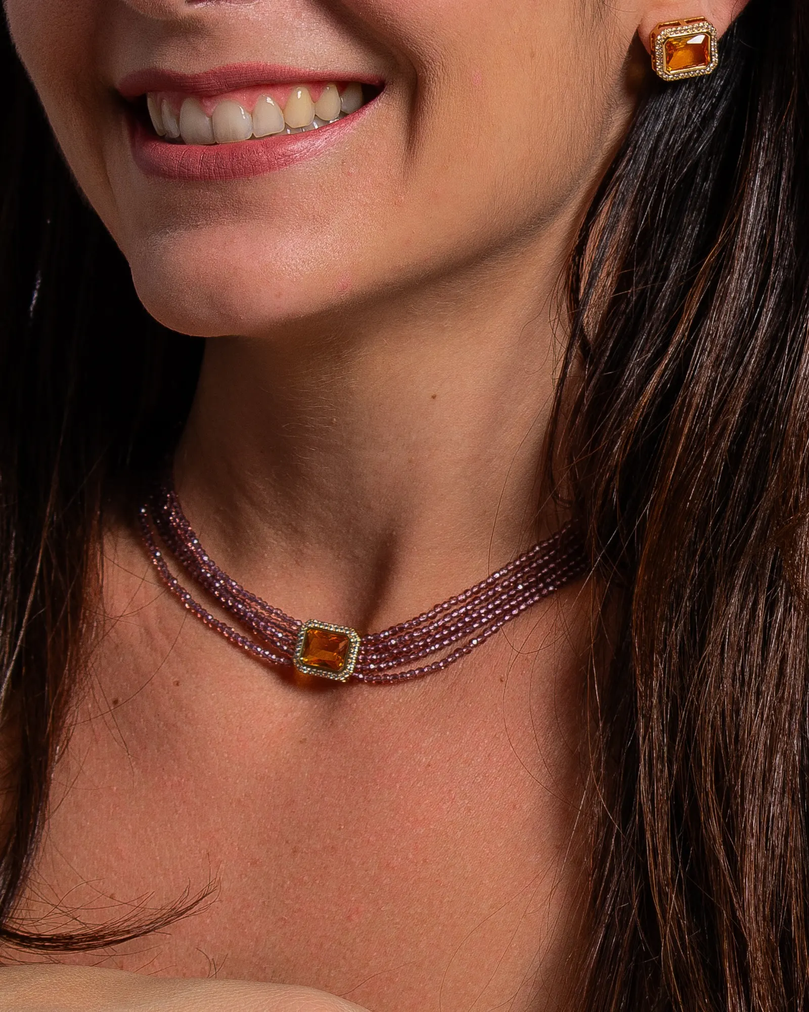 Modelo sorrindo usando choker de pedras vermelhas com pingente