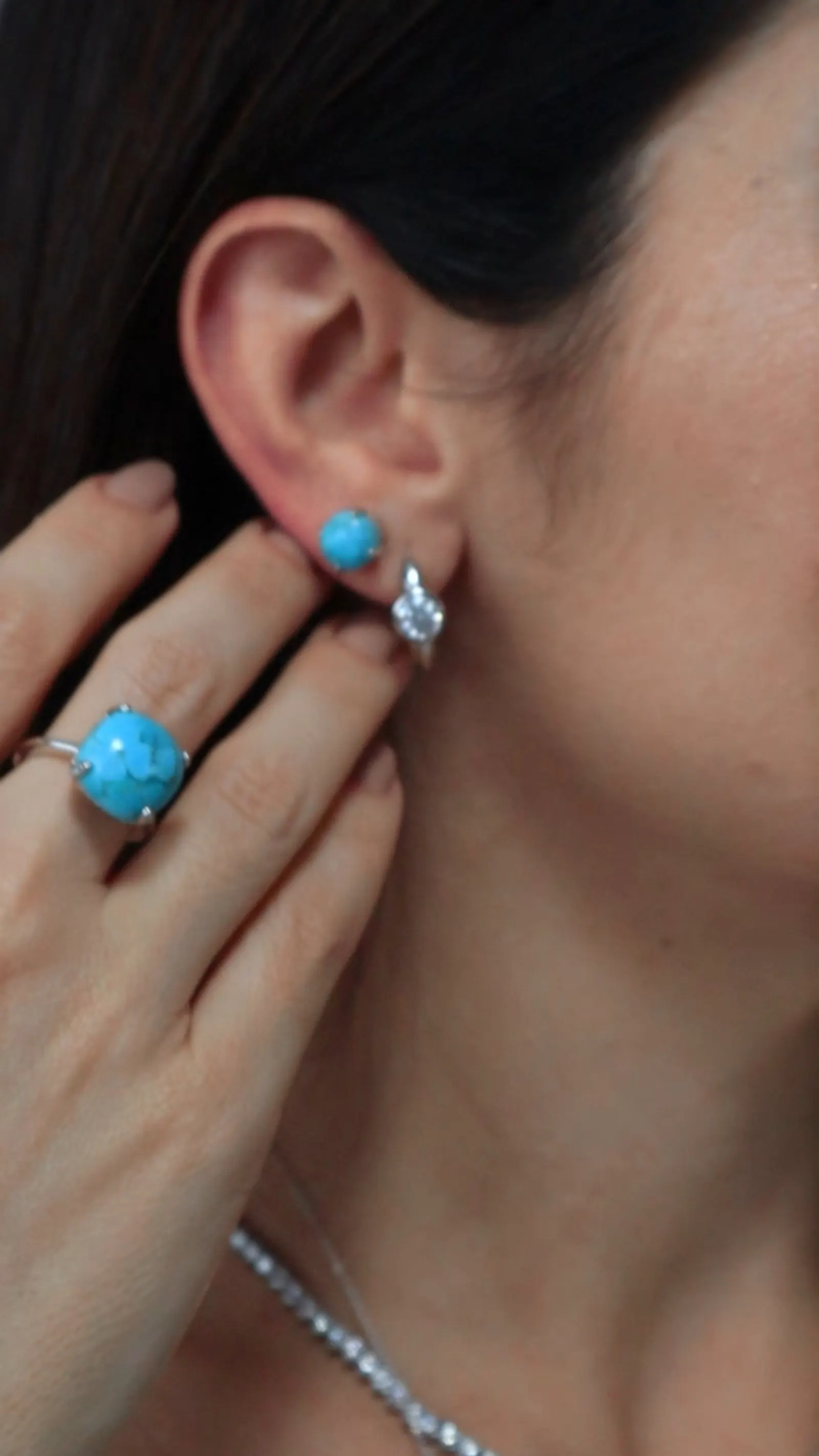 Mão com anel de pedra turquesa junto à orelha com brinco